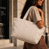 Canvas tote tas in off-white met brede hengsels en subtiel logo op de voorkant.