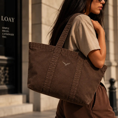 Canvas tote tas in bruin met brede hengsels, doorgestikte naden en klein logo.