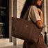 Canvas tote tas in bruin met brede hengsels, doorgestikte naden en klein logo.