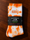 Paar tie-dye sokken wit en oranje met label KUDOS en Swirly Sox op de band.